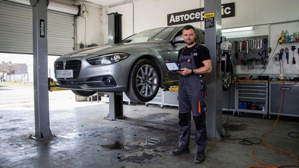 Vehicle on a lift inside a network workshop bay while a technician runs a diagnostic scan